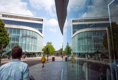 Exeter, Devon, İngiltere. 08-05-25. John Lewis mağaza önünde parlak mavi bir gökyüzü karşı. Sağ tarafta güçlü bir yansıma simetrik bir denge sağlar. Perakende satışları. Ana Cadde. 