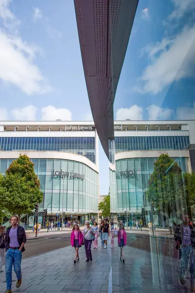 Exeter, Devon, İngiltere. 08-05-25. John Lewis mağaza önünde parlak mavi bir gökyüzü karşı. Sağ tarafta güçlü bir yansıma simetrik bir denge sağlar. Perakende satışları. Ana Cadde. 