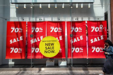 Exeter, Devon, İngiltere. 05-08-25. % 70 'e varan indirimli pankartlar. Parlak kırmızı göz, sarı bir pencere etiketi ile görüntüyü yakalıyor. İndirim, satış ve fiyat indirimi perakende imajı.