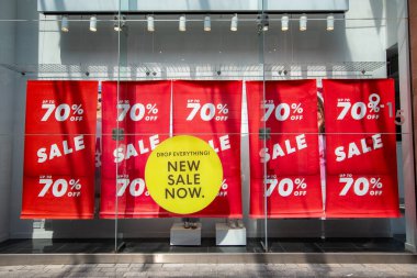 Exeter, Devon, İngiltere. 05-08-25. % 70 'e varan indirimli pankartlar. Parlak kırmızı göz, sarı bir pencere etiketi ile görüntüyü yakalıyor. İndirim, satış ve fiyat indirimi perakende imajı.