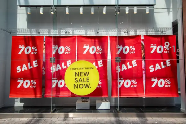 Exeter, Devon, İngiltere. 05-08-25. % 70 'e varan indirimli pankartlar. Parlak kırmızı göz, sarı bir pencere etiketi ile görüntüyü yakalıyor. İndirim, satış ve fiyat indirimi perakende imajı.