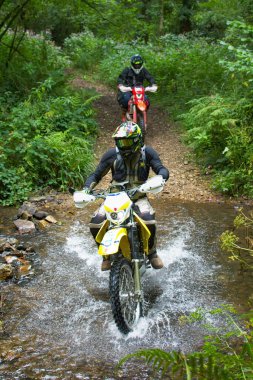 Exeter, Devon, İngiltere. 08-07-25. Bir off road denemesi bisikleti, lastiklerinden su damlayan bir dereden geçer. Motosiklet sporu ve eğlence. Grönland. 
