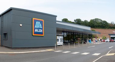 Torquay, Devon, uk. 08-14-25. Geniş açı panoramasında Aldi süpermarketi. Görüntü ön cephede Aldi logosu ve girişe yaklaşan müşterileri ve arkada kalabalık bir otoparkı gösteriyor.. 
