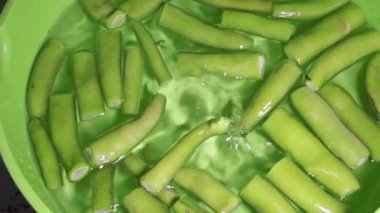 Beyaz plastik kasede taze fasulye doğrayan bir kadın..