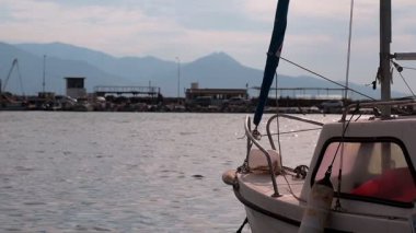 Marinadaki sakin denizde bir tekne yavaşça sallanıyor. Karşı kıyıda balıkçı tekneleri ve yüksek dağlar var..