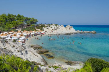 Mega Portokali Plajı 08-05-2023 Yunanistan, Halkidiki, Sithonia. Plaj şemsiyeleri, beyaz kayaları, masmavi gökyüzü olan bir sürü insan.