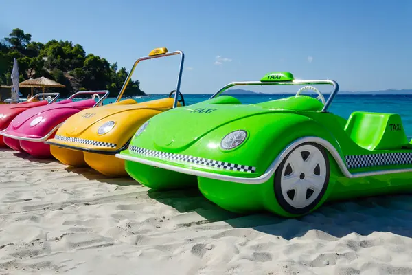 pedal catamarans in shape of car lined up in row. boats of different colors standing on sand