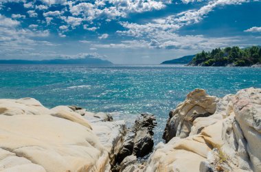 Halkidiki 'deki Karidi gölünde beyaz doğal mermer. Gök mavisi deniz, arka planda başka bir yarımadanın dağlık kıyıları ve bulutlu gökyüzü.
