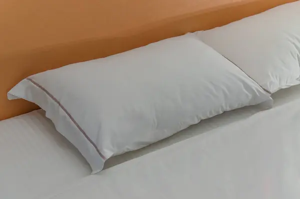 White pillows on white sheets. Wooden headboard in Background
