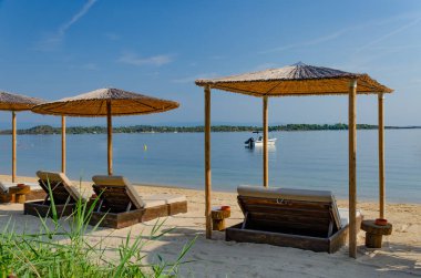 Saman şemsiyelerin altında yatakları olan temiz bir sahil. Tekneyle sakin koy. Önplanda çim.