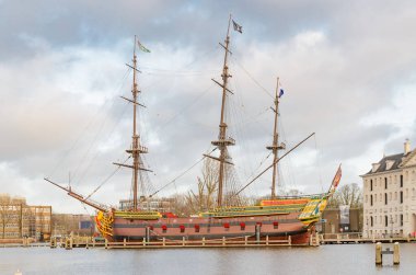 Büyük, üç direkli bir kopya gemi tarihi bir binanın yanındaki limana yanaştı. Amsterdam 'da ahşap firkateyn.