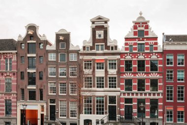 Amsterdam 'da tarihi gable-çatılı kanal evleri. Kahverengi, koyu kırmızı, turuncu binalar zengin bir şekilde beyaz sıva ile süslenmiş..