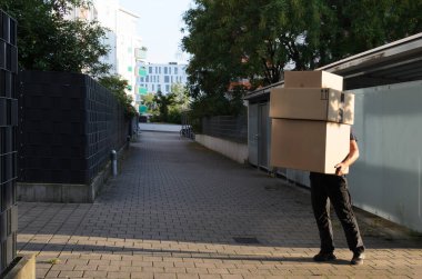 Teslimatçı büyük kutuları tutuyor. Kafasını kutuların arkasında göremezsin. Kafkasyalı, tam yükseklikte duruyor. O, bir kasaba evinin avlusunda. Güneş ışığı kutuların üzerine düşüyor..