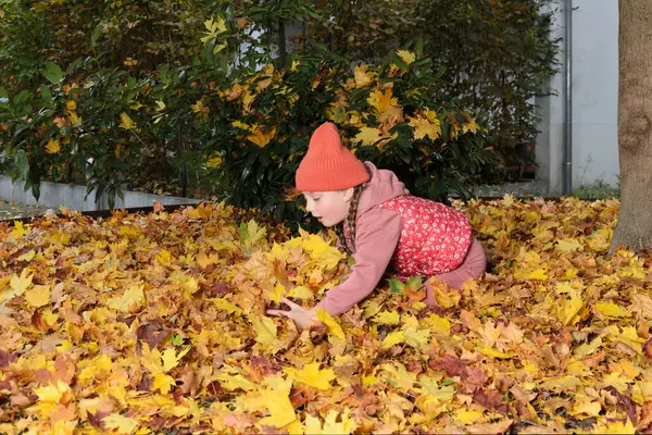 Bir çocuk düşmüş sarı akçaağaç yapraklarıyla oynuyor. Kız altı yaşında ve iki sarı örgülü saçı var. Onun kafasında bir kep var. Bir çocuk dökülen yapraklara oturur..