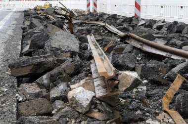Yıkılmış bir tramvay hattına yakından bakıldığında bükülmüş metal raylar, kırık asfalt ve beton döküntüler görülüyor. Arka planda beyaz güvenlik bariyerleri görülüyor. Bu da devam eden kentsel inşaatı gösteriyor..