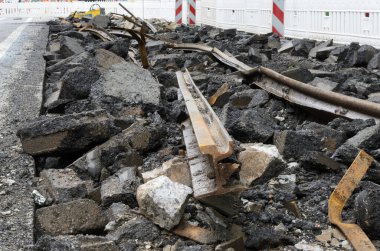 Yıkılmış bir tramvay hattına yakından bakıldığında bükülmüş metal raylar, kırık asfalt ve beton döküntüler görülüyor. Arka planda beyaz güvenlik bariyerleri görülüyor. Bu da devam eden kentsel inşaatı gösteriyor..