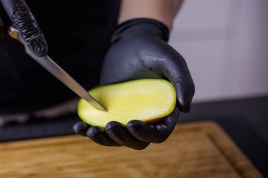 Siyah eldivenli biri meyve suyu için mango kesiyor ve kesiyor. Yüksek kalite fotoğraf