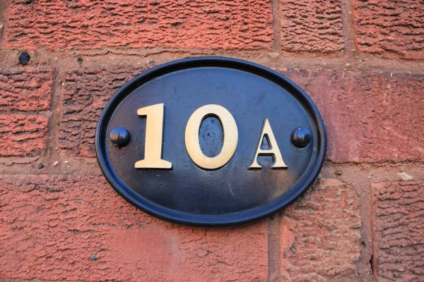 Number 10 A black door sign with gold coloured text attached to a brick wall