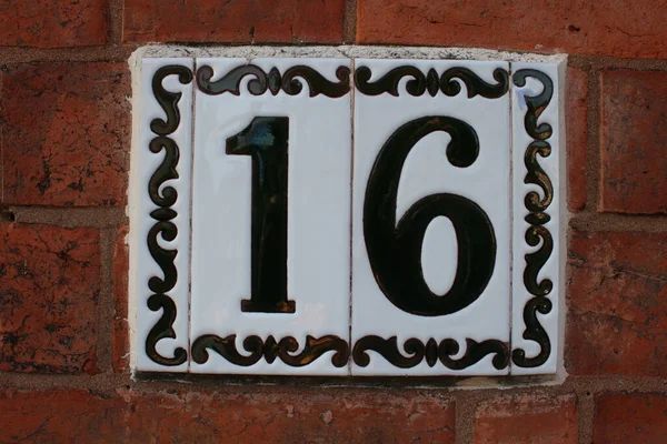 Number 16 door number Ceramic plate with black decorative boarder attached to a brick wall