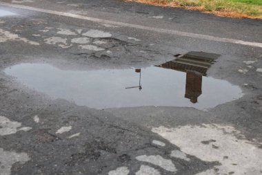 Yerde su birikintisi, bir ev bacası ve televizyon antenini gösteren yansıma. 