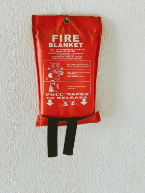 Beyaz duvarda asılı kırmızı bir itfaiye battaniyesi.