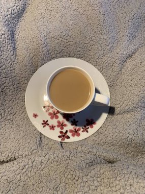 Bir fincan kahve ve yatağında kırmızı pembe çiçekler olan bir fincan çay tabağı.