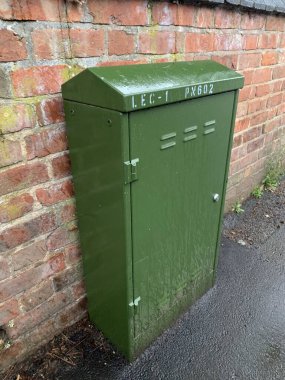 Yeşil fiber iletişim dolabı halka açık bir kaldırımda, tuğla bir duvara dayalı, bulutlu bir öğleden sonra çekildi.