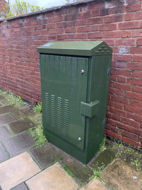 Yeşil fiber iletişim dolabı halka açık bir kaldırımda, tuğla bir duvara dayalı, bulutlu bir öğleden sonra çekildi.