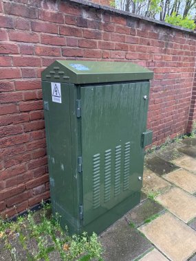 Yeşil fiber iletişim dolabı halka açık bir kaldırımda, tuğla bir duvara dayalı, bulutlu bir öğleden sonra çekildi.