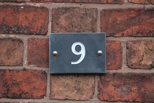Number nine door metal house sign in white, number engraved into metal with brick wall in background