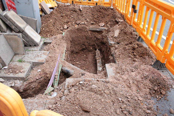 Дорожные работы, вырытые тротуары с открытой трубой и электрические кабели и желтый пластиковый барьер, большая дыра в тротуаре