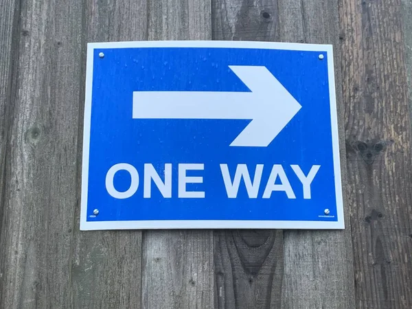 Up close picture of a UK one way sign attached to a wooden fence