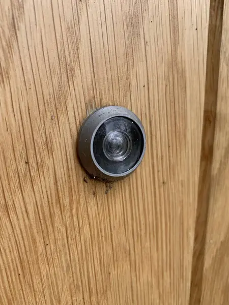 Close up picture of a door peep hole attached to a wooden door
