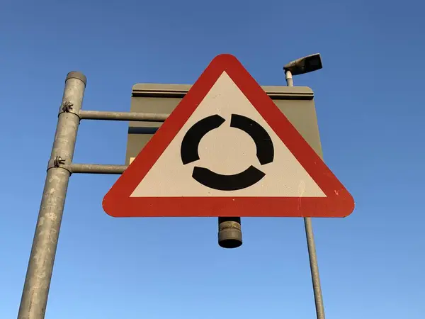 UK roundabout ahead warning sign against a clear blue sky, roundabout road sign