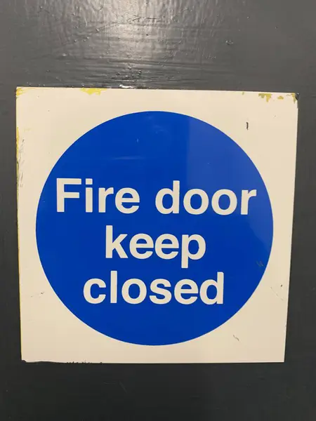 Fire door keep shut sign, Up close picture attached to a grey painted wooden door