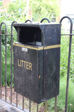 Kamu parkındaki siyah metal çöp tenekesi, metal kapıya takılan çöp tenekesi.