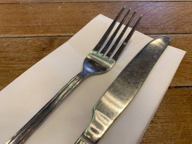 Kağıt peçetenin üzerinde çatal ve bıçak, ahşap masanın üstünde açı ile çekilmiş fotoğraf.