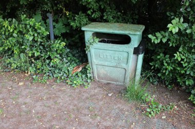 Halka açık bir parkta çekilmiş eski yeşil metal kutu, arka planda çalılar.