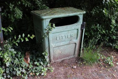 Halka açık bir parkta çekilmiş eski yeşil metal kutu, arka planda çalılar.