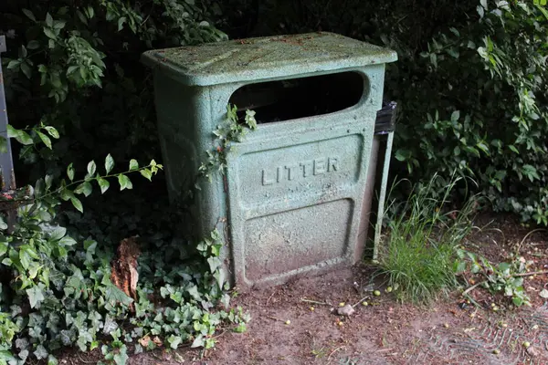 Halka açık bir parkta çekilmiş eski yeşil metal kutu, arka planda çalılar.