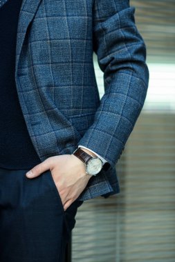 Pahalı bir iş elbisesi içinde, eli cebinde üst düzey bir kol saati olan bir adamın kısmi görüntüsü..