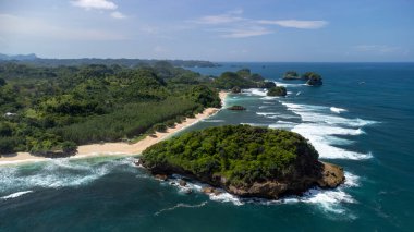 Kıyı şeridinin görünümü temiz ve düz, beyaz kum ve büyük dalgalarla esniyor.