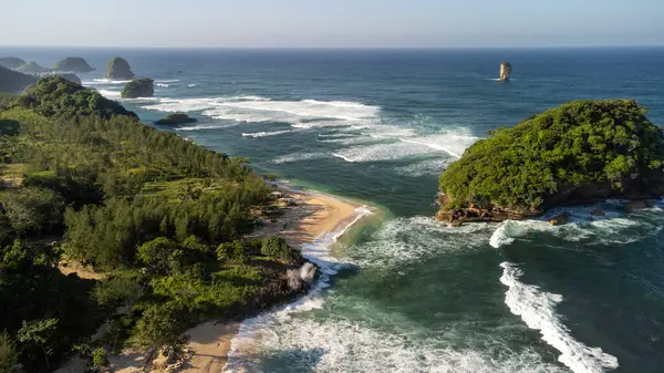 Endonezya 'daki Tanjung Penyu Mas Sahili' nde yeşil ağaçlarla kaplı küçük bir ada ve çok büyük dalgalar var.