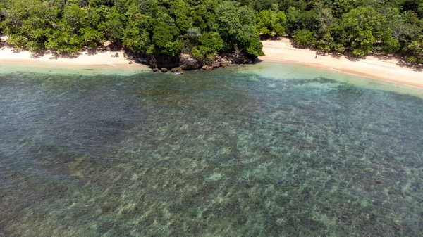 Plajın dibindeki hava manzarası bir sürü siyah mercan ve küçük dalgaları gösteriyor. Burası Kondang Merak Sahili, Doğu Java.