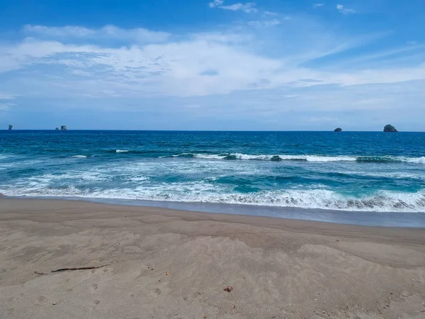 Jolangkung plajı, mavi sahil suyu, mavi gökyüzü ve biraz sarı kum.
