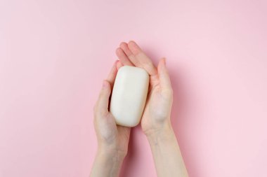 Kadının elleri pastel pembe arka planda sabun tutuyor. Üst manzara, düz uzanma.