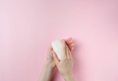 Kadının elleri pastel pembe arka planda sabun tutuyor. Üst manzara, düz uzanma.