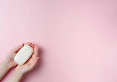 Kadının elleri pastel pembe arka planda sabun tutuyor. Üst manzara, düz uzanma.