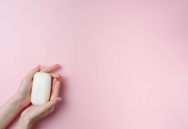 Kadının elleri pastel pembe arka planda sabun tutuyor. Üst manzara, düz uzanma.