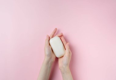 Kadının elleri pastel pembe arka planda sabun tutuyor. Üst manzara, düz uzanma.